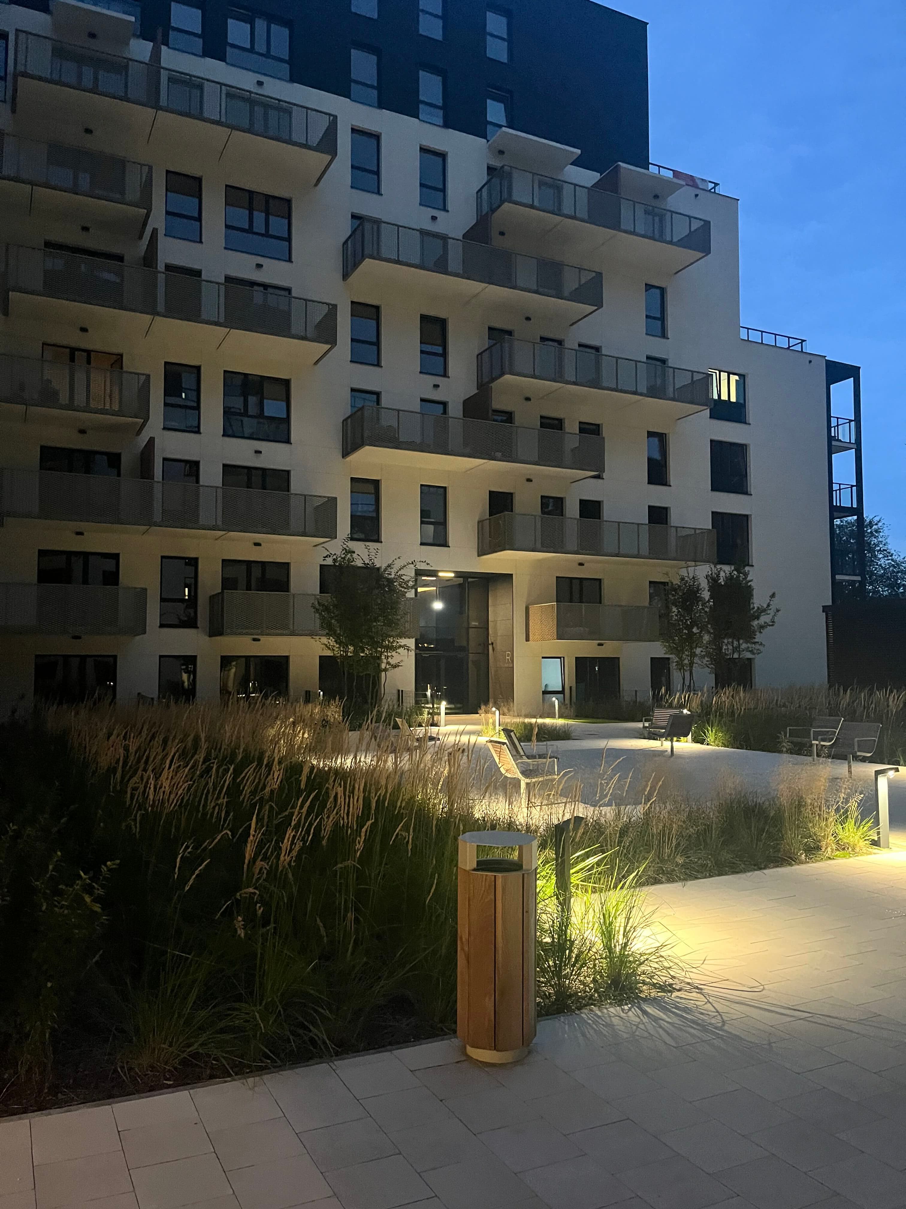 Illuminated courtyard seating and ornamental grasses at the building entrance.