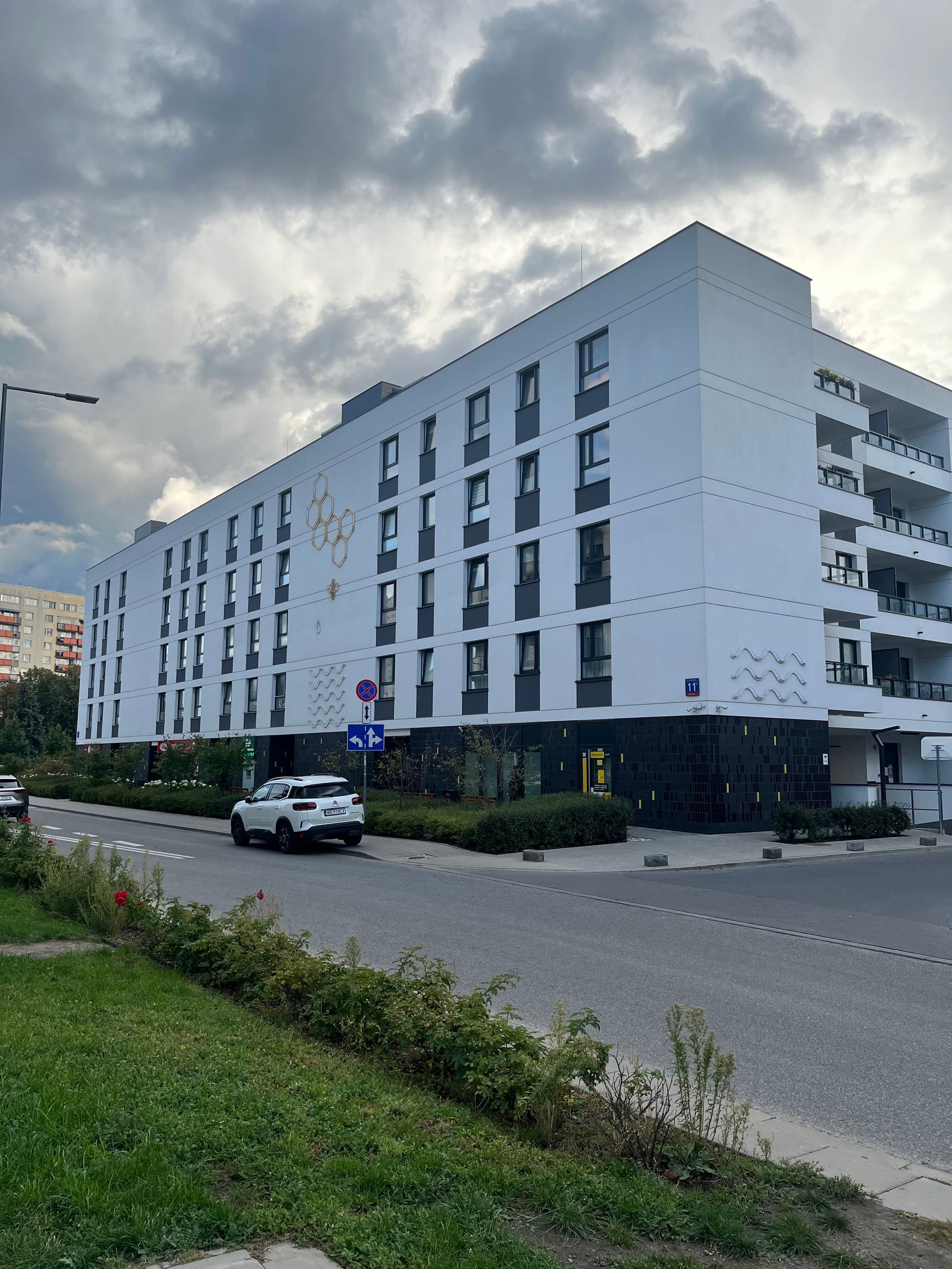 Neowo corner building with honeycomb mural, bee emblem, and ground-floor Żabka (plate 11).