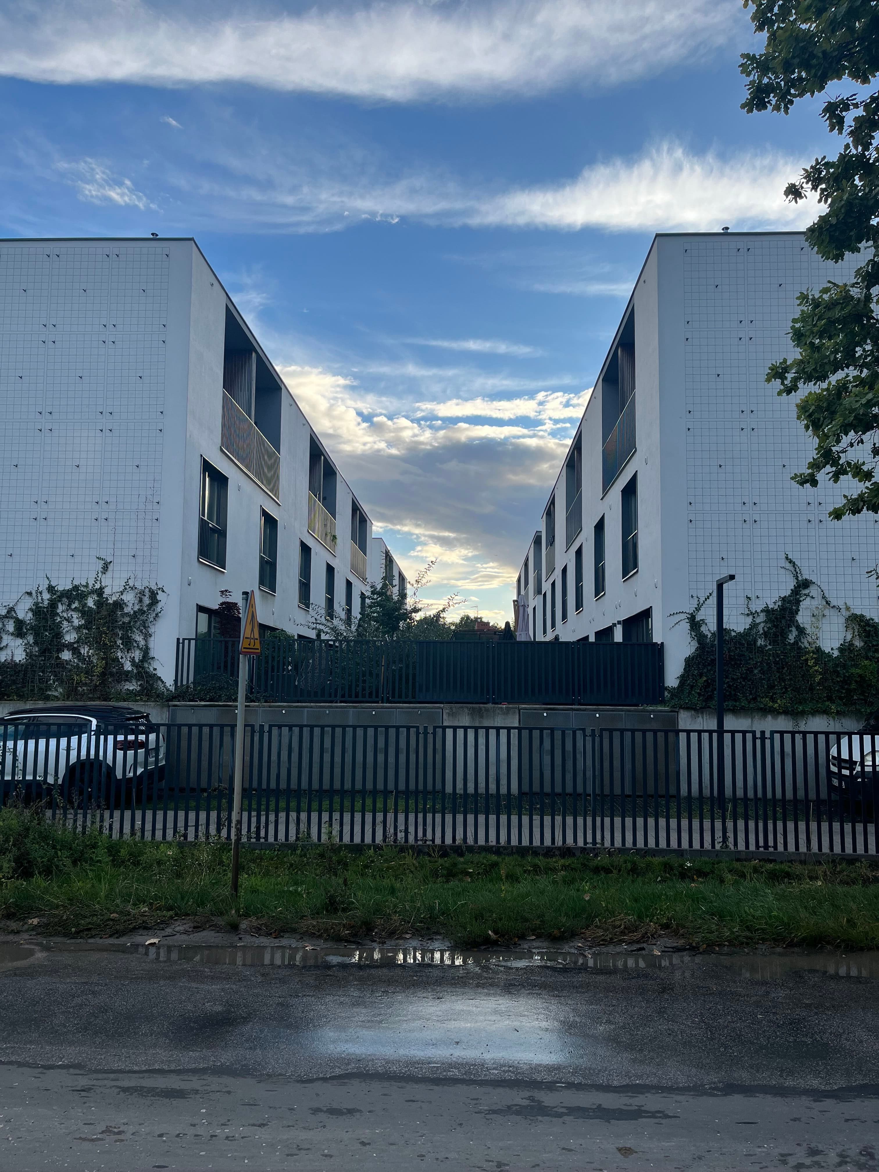 Street view into Villa De Charme — white tiled end walls, climbing greenery and metal fence on Szeligowska.