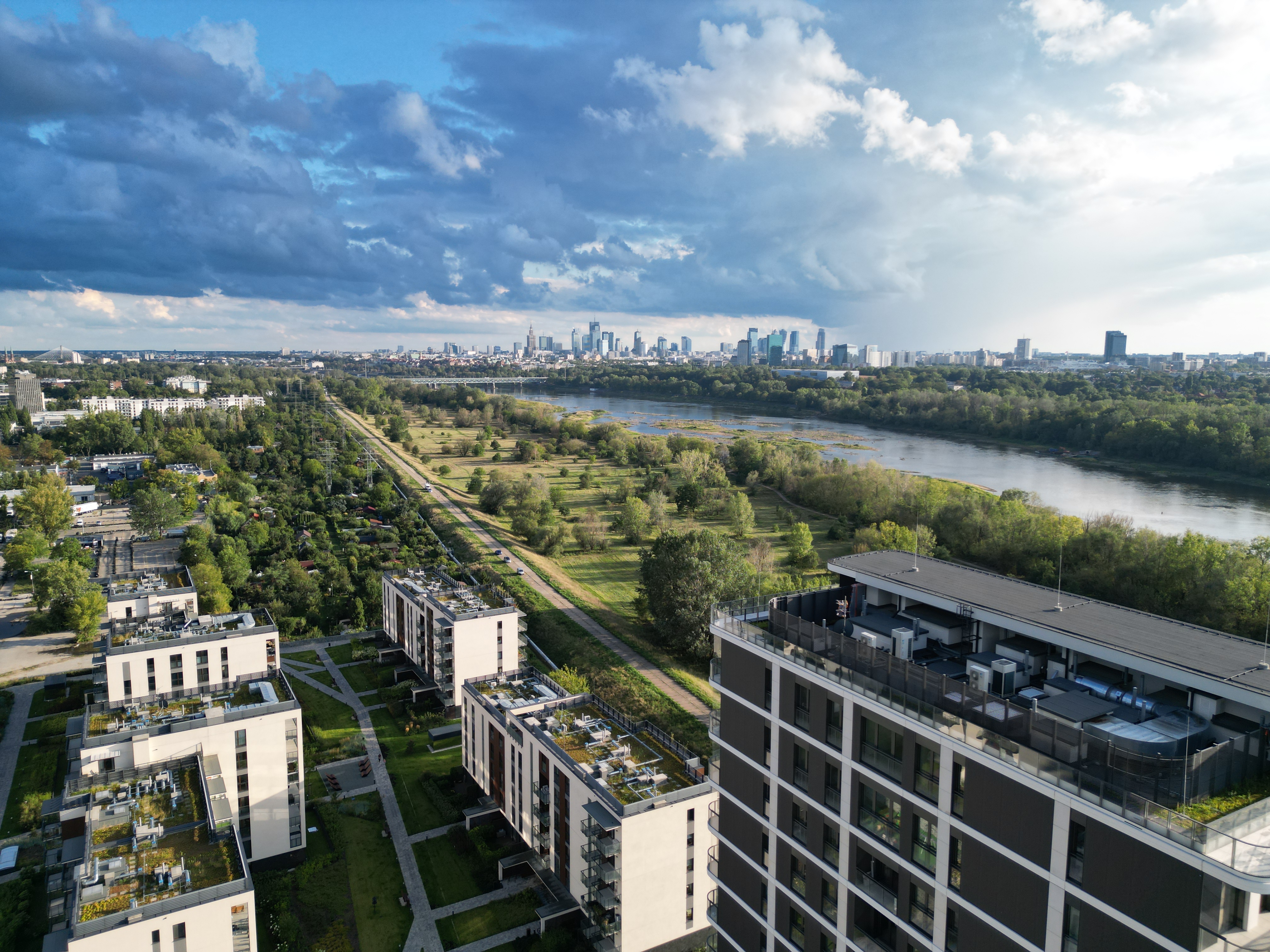 Aerial view of Bulwary Praskie along the Vistula, with the finished blocks, the wild riverbank, and Warsaw’s skyline beyond