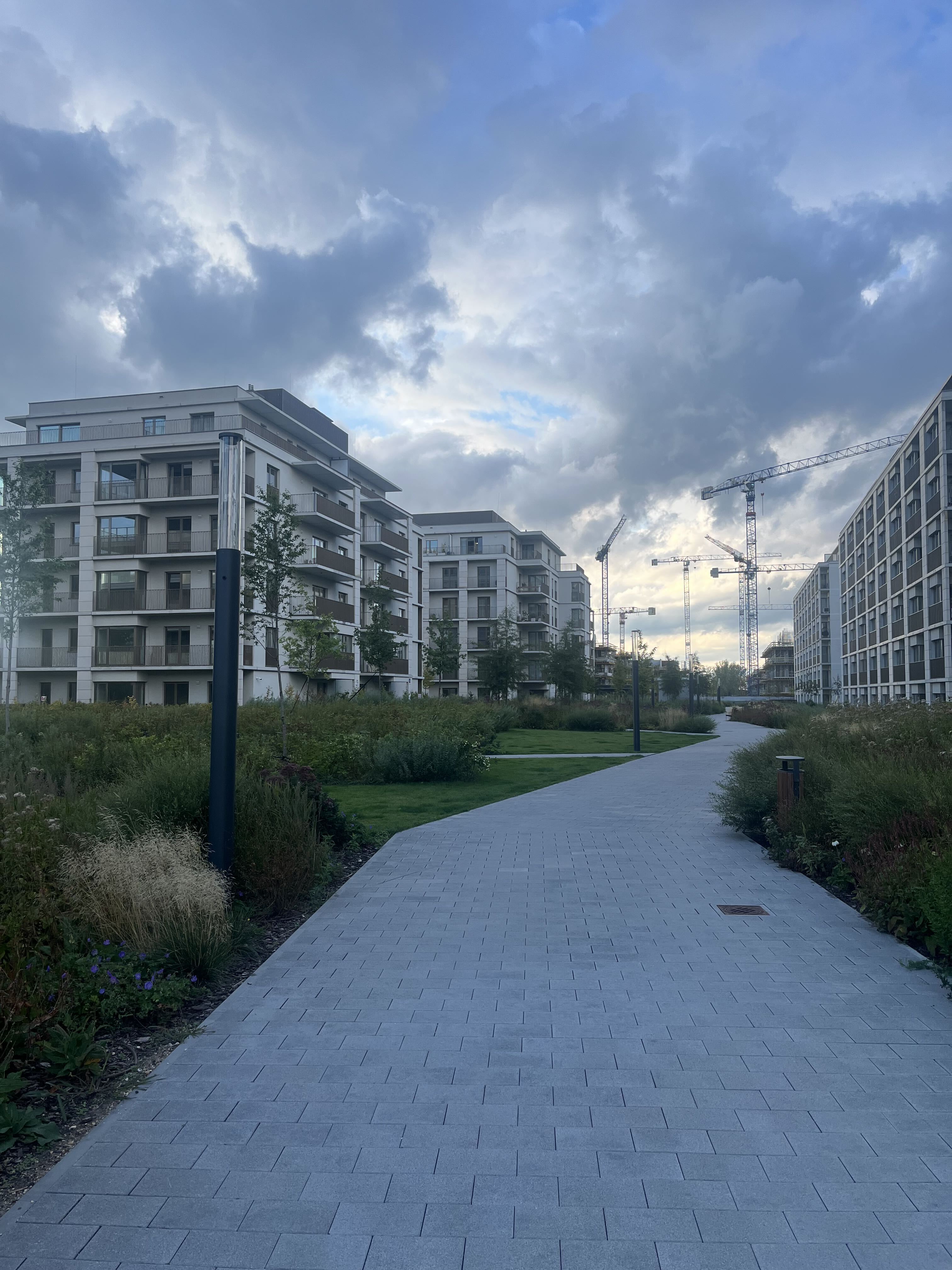 Path through a finished phase of Bulwary Praskie, with cranes on the next stage behind the blocks