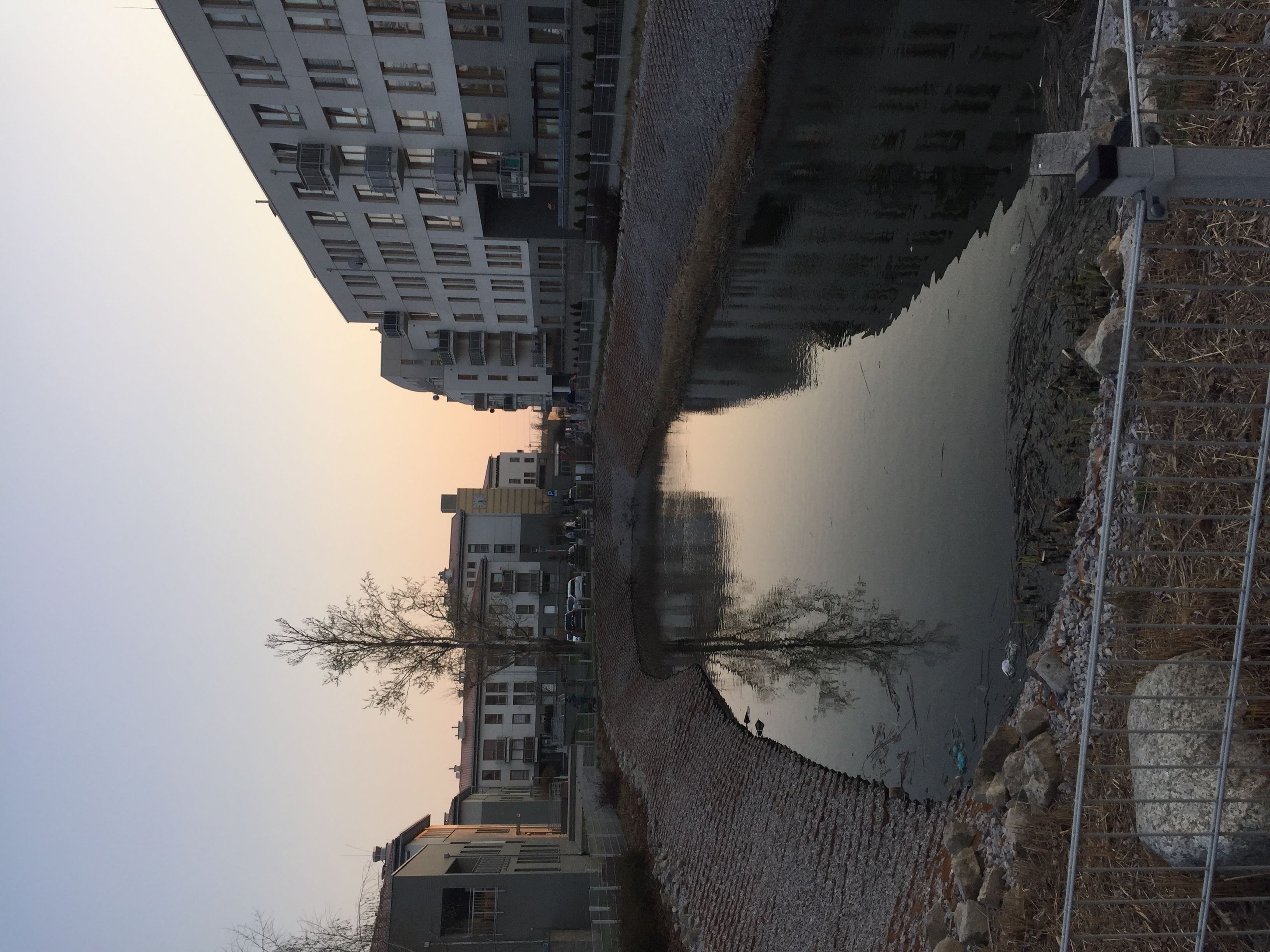 Artificial lake at Zielona Italia at dusk, with gabion banks and apartment buildings around it